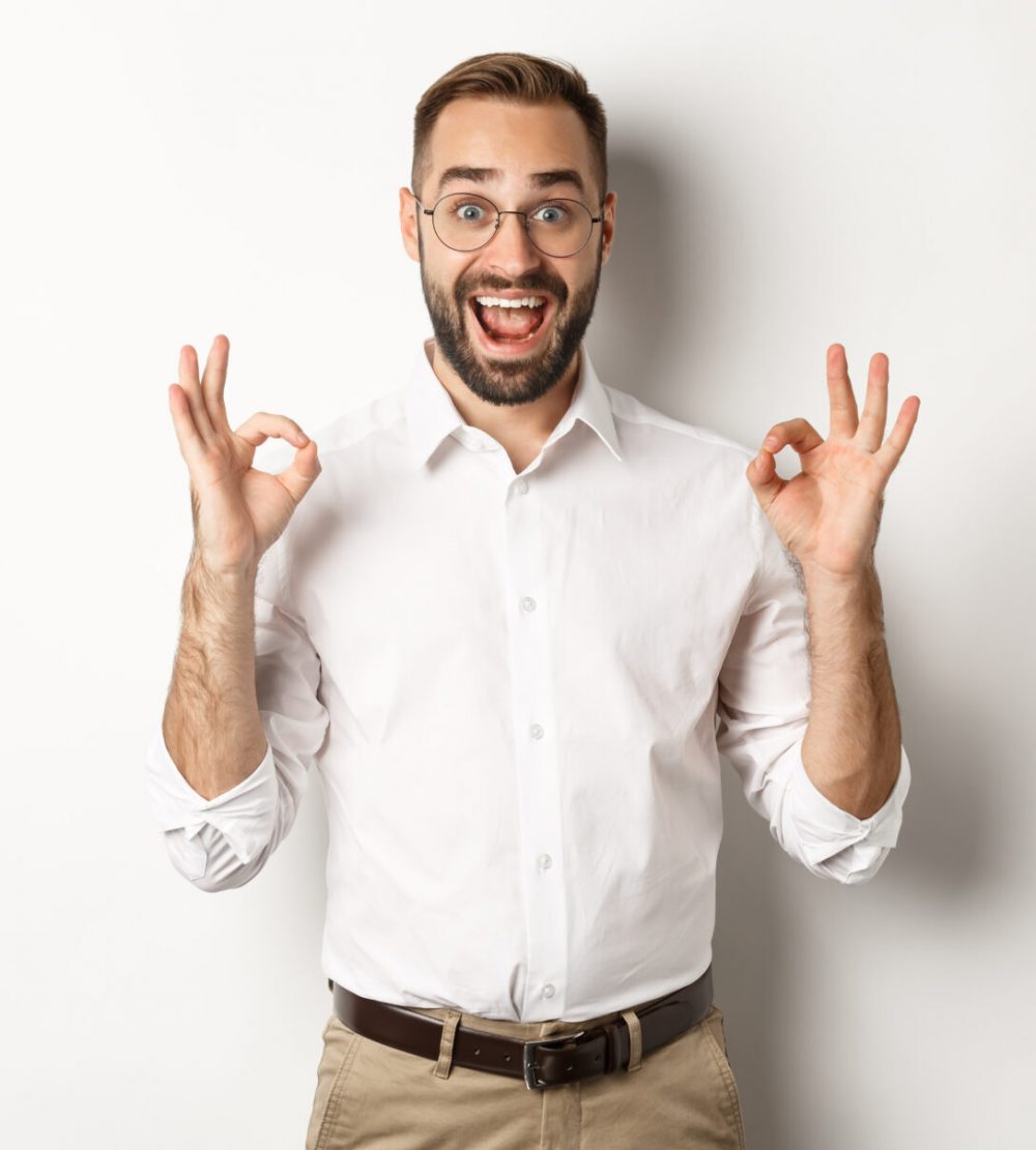 Amazed entrepreneur showing okay sign and looking happy, satisfied with product, standing over white background. Copy space